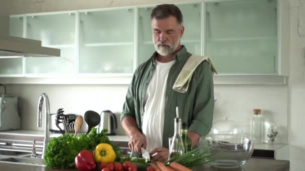 Starší šťastný muž připravuje zdravé jídlo doma, krájení čerstvý zeleninový salát stojící v moderní kuchyni interiéru. — Stock video
