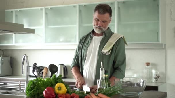 Starší šťastný muž připravuje zdravé jídlo doma, krájení čerstvý zeleninový salát stojící v moderní kuchyni interiéru. — Stock video