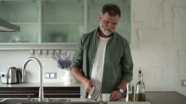 Mutfakta duran kıdemli adam kahve doldurup kahve içiyor.