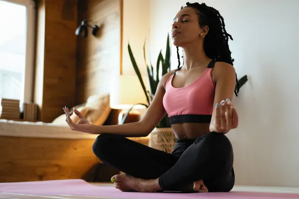 Ung svart kvinna som gör yoga hemma i lotusposition. — Stockfoto