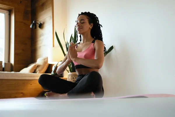 Jonge zwarte vrouw doet yoga thuis in de lotus positie. — Stockfoto