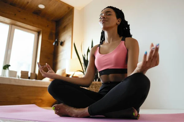 Ung svart kvinna som gör yoga hemma i lotusposition. — Stockfoto