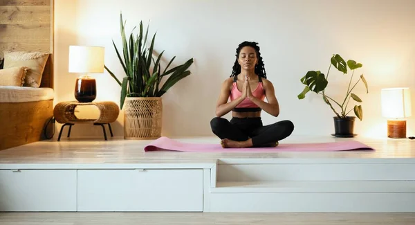 Ung svart kvinna som gör yoga hemma i lotusposition. — Stockfoto