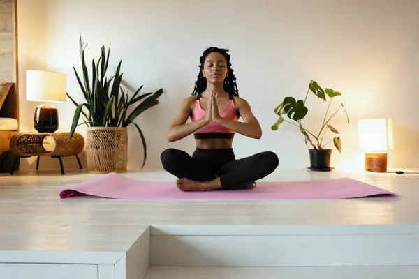 Joven mujer negra haciendo yoga en casa en la posición de loto. — Foto de Stock