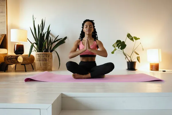 Ung svart kvinna som gör yoga hemma i lotusposition. — Stockfoto