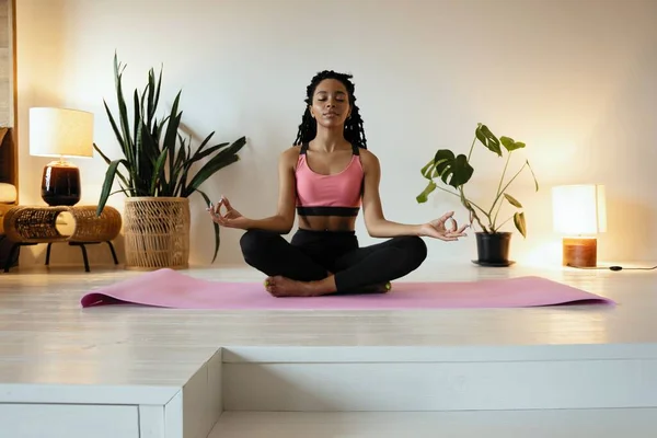 Ung svart kvinna som gör yoga hemma i lotusposition. — Stockfoto