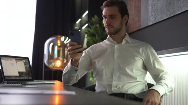 Male millennial professional holding smartphone texting message in office using helpful mobile apps for business — Stock Video