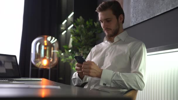 Erkek milenyum profesyoneli ofiste akıllı telefon mesajı tutuyor. İş için yararlı cep telefonu uygulamaları kullanıyor. — Stok video