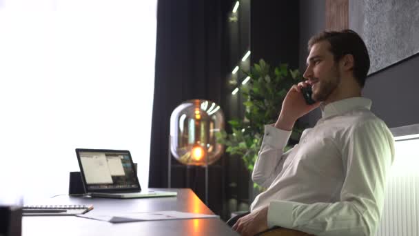 Glimlachende jonge volwassene professionele casual zakenman het maken van business call praten op de smartphone in het kantoor — Stockvideo