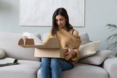 Kızgın, kafası karışık bir kadın paketleri açıyor, yanlış ya da bozuk bir online mağaza siparişi. Kötü teslimat servisi