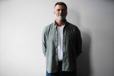 Beyaz arka planda duran gülümseyen olgun bir adamın portresi.