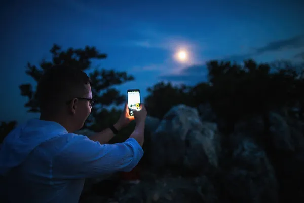 Le concept d'astrophotographie mobile un jeune homme photographie la lune sur son téléphone — Photo