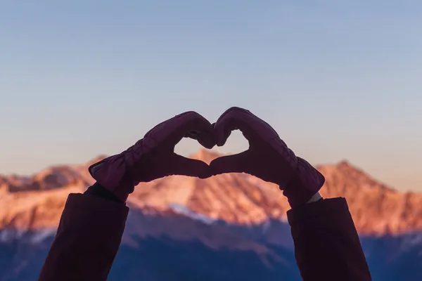 Mujer haciendo forma de corazón con las manos sobre montañas nevadas en el crepúsculo de invierno — Foto de Stock