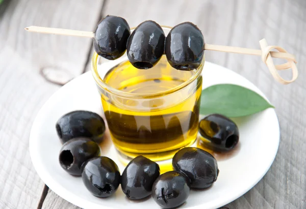 Teller mit Oliven und einer Flasche Olivenöl auf einem Holzgrund — Stockfoto