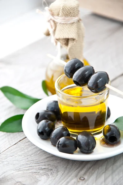 Plaat met olijven en een fles olijfolie op een houten achtergrond — Stockfoto