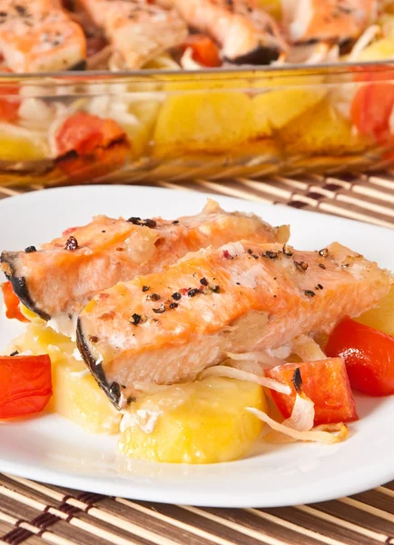 Stukken van zalm met aardappelen, tomaten en uien gebakken in de oven — Stockfoto