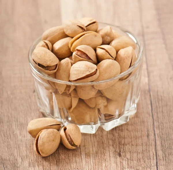 Pistachos en un recipiente de vidrio sobre un fondo de madera — Foto de Stock