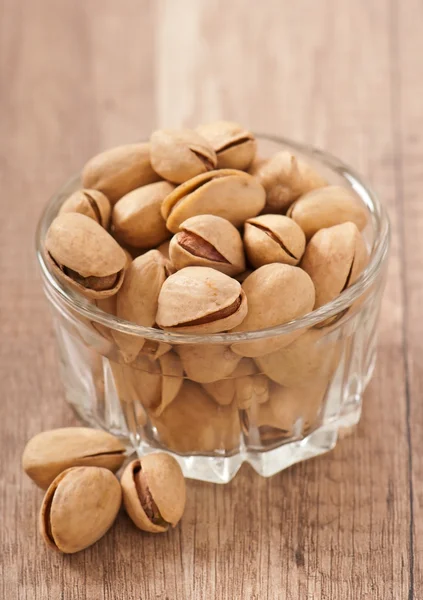 Pistachos en un recipiente de vidrio sobre un fondo de madera — Foto de Stock