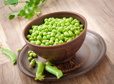 Green peas in a ceramic bowl on old wooden background clipart