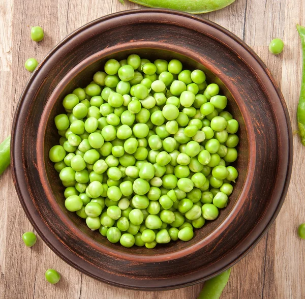 Green peas in a ceramic bowl on old wooden background — Stock Photo, Image
