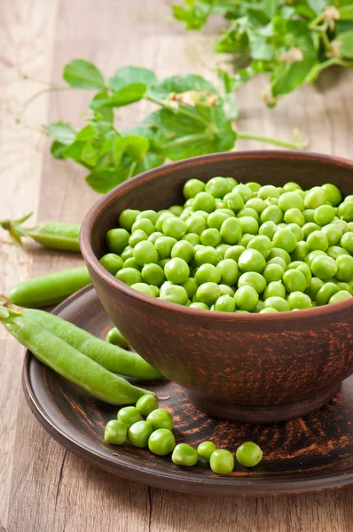 Green peas in a ceramic bowl on old wooden background — Stock Photo, Image