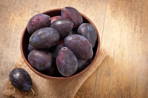 Plums in bowl on wooden table — Stock Photo, Image