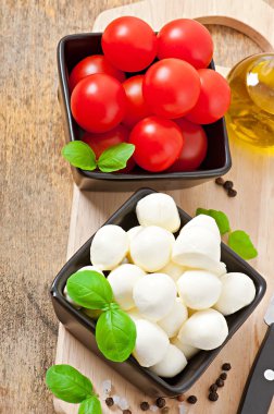 Mozzarella peyniri, domates ve taze fesleğen yaprakları üzerinde ahşap arka plan