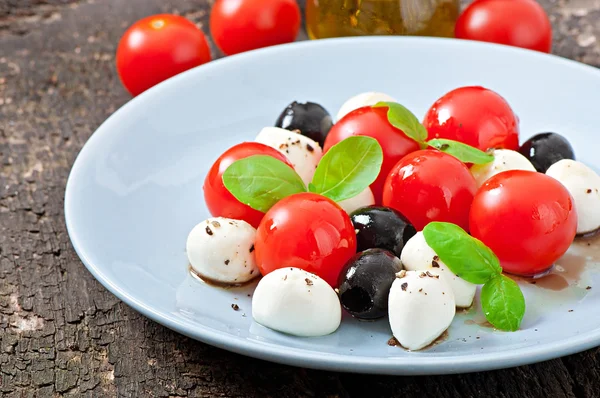 Świeże sałatki z pomidorów cherry, bazylia, mozzarella i czarnymi oliwkami. — Zdjęcie stockowe