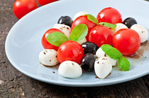 Świeże sałatki z pomidorów cherry, bazylia, mozzarella i czarnymi oliwkami. — Zdjęcie stockowe