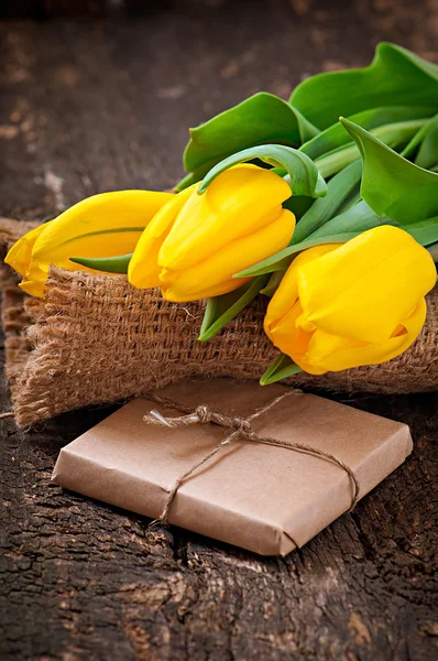 Bouquet of yellow tulips and chocolate wrapping paper on wooden background — Stock Photo, Image