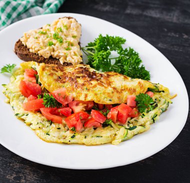 Kahvaltıda. Kabaklı omlet, peynir ve domates salatası ve beyaz tabakta sandviç. Frittata - İtalyan omleti.