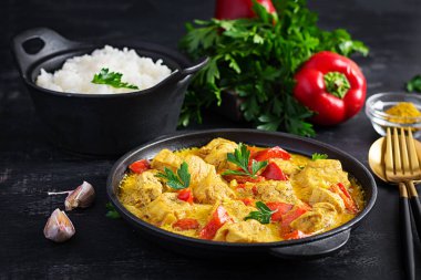 Geleneksel Hint körili tavuk masalası. Hint usulü körili tatlı biberli tavuk ve kase içinde pilav, baharatlar, koyu arka plan. Geleneksel Hint yemeği.