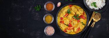 Geleneksel Hint körili tavuk masalası. Hint usulü körili tatlı biberli tavuk ve kase içinde pilav, baharatlar, koyu arka plan. Geleneksel Hint yemeği. Üst görünüm, afiş