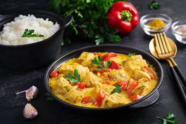 Geleneksel Hint körili tavuk masalası. Hint usulü körili tatlı biberli tavuk ve kase içinde pilav, baharatlar, koyu arka plan. Geleneksel Hint yemeği.