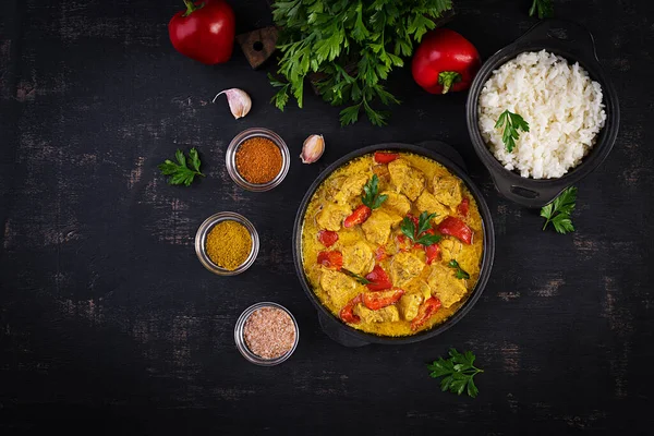 Geleneksel Hint körili tavuk masalası. Hint usulü körili tatlı biberli tavuk ve kase içinde pilav, baharatlar, koyu arka plan. Geleneksel Hint yemeği. Üst manzara, düz uzanma