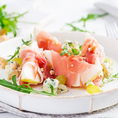 Beyaz bir tabakta armut, mavi peynir ve jambonlu aperatif..