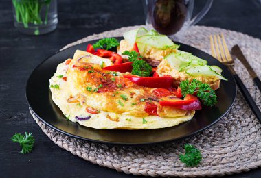 Kahvaltıda. Kırmızı biberli omlet, peynirli ve siyah tabakta sandviçli domates. Frittata - İtalyan omleti.