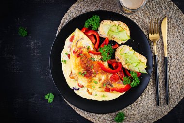 Kahvaltıda. Kırmızı biberli omlet, peynirli ve siyah tabakta sandviçli domates. Frittata - İtalyan omleti. Üst görünüm, yukarıda