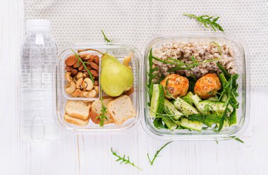 Beslenme çantası yulaf ezmesi, salatalık salatası, ve fındık, ekmek, beyaz ahşap arka planda armut. Beslenme çantası yemeği. Üst manzara, düz uzanma