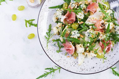 Armut salatası, mavi peynir, üzüm, prosciutto, roka ve hafif arkaplanda baharatlı sos. Sağlıklı beslenme. Üst görünüm, genel görünüm