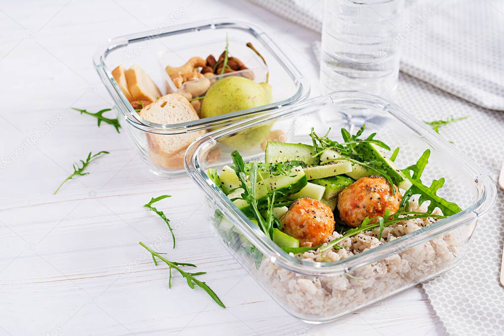 Lunch box filled with oatmeal, cucumber salad, and nuts, bread, pear on white wooden background. Lunchbox dinner.
