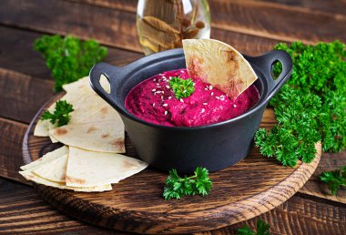 Ahşap arka planda siyah bir kasede pide ile kavrulmuş pancar humusu..