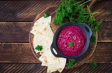 Ahşap bir arka planda siyah bir kasede pide ile kavrulmuş pancar humusu. Üst görünüm