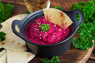 Ahşap arka planda siyah bir kasede pide ile kavrulmuş pancar humusu..