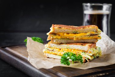 Kızarmış sandviç peyniri ve çırpılmış yumurta kağıt üzerinde ve tahta tahtada da kahve bardağı. Koyu arkaplan.