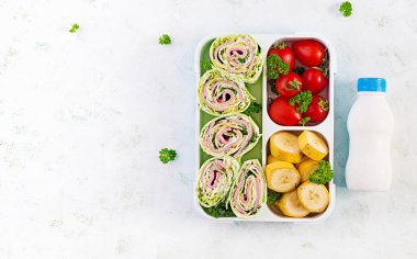 Okul beslenme çantası. Tortilla ambalajlı, domatesli, muzlu ve yoğurtlu sağlıklı beslenme çantası. Üst manzara, düz uzanma