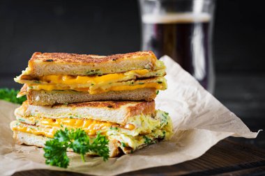 Kızarmış sandviç peyniri ve çırpılmış yumurta kağıt üzerinde ve tahta tahtada da kahve bardağı. Koyu arkaplan.