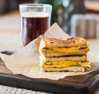 Kızarmış sandviç peyniri ve çırpılmış yumurta kağıt üzerinde ve tahta tahtada da kahve bardağı. Koyu arkaplan.