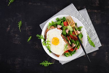 Kahvaltı - kızarmış yumurtalı tost ve yeşillikli domates salatası ve koyu arkaplanda morina ciğeri. Sağlıklı kahvaltı. Üst görünüm