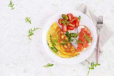 Kahvaltıda. Peynirli omlet, yeşil roka ve beyaz tabakta somonlu sandviç. Frittata - İtalyan omleti. Üst görünüm